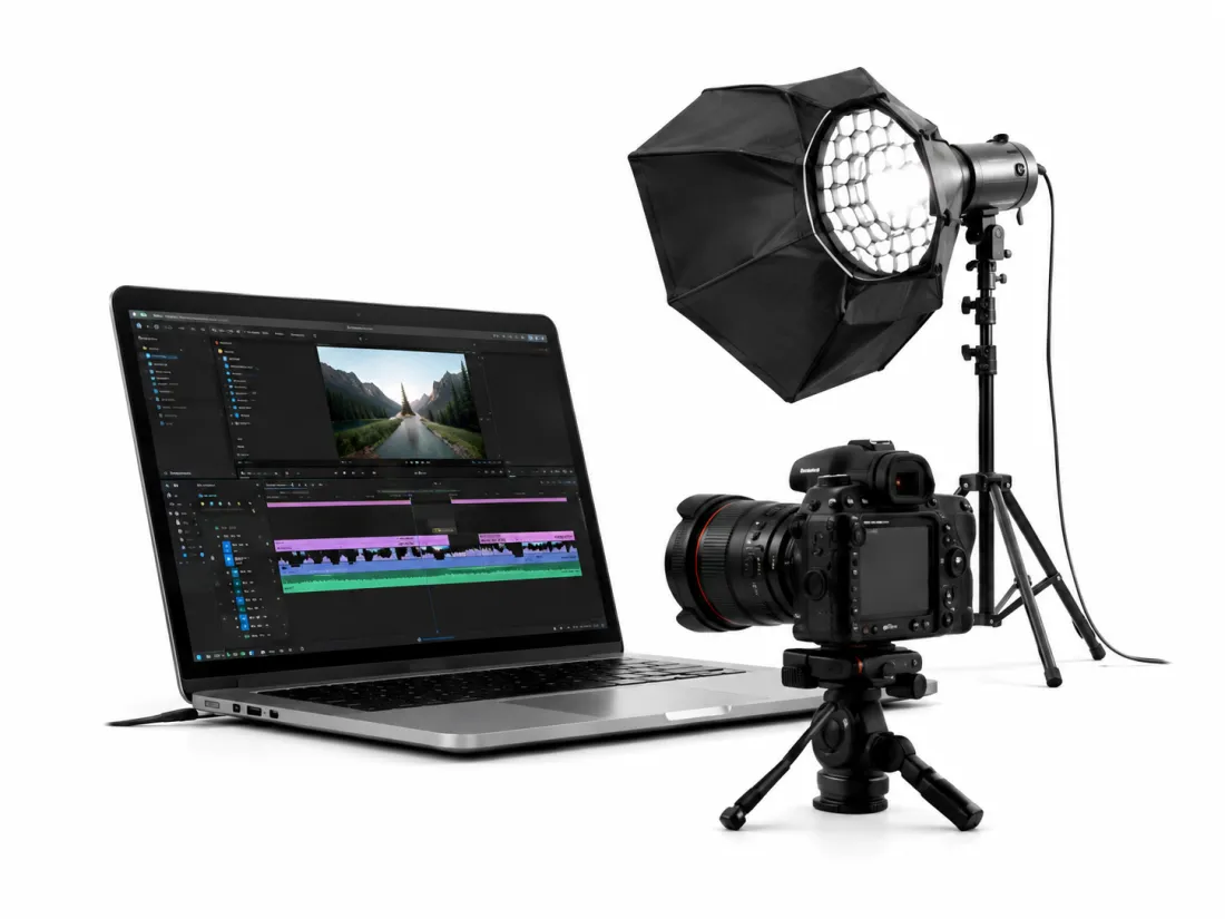 A laptop running a video edit timeline beside a camera on a tripod and a softbox light